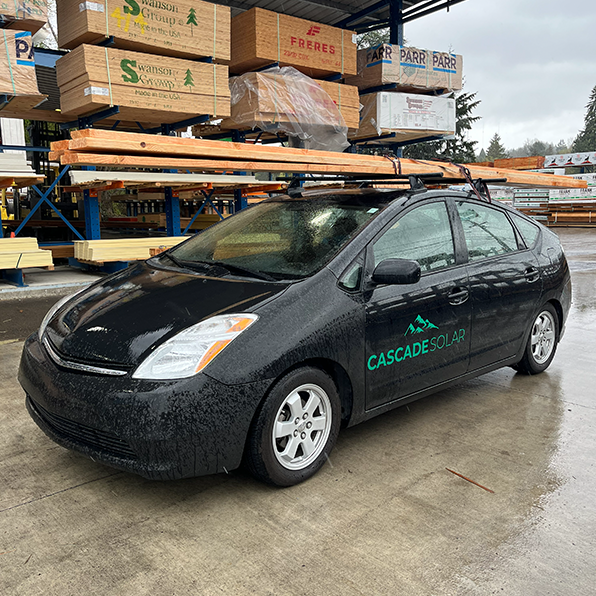 Cascade Solar Prius parked at a lumber yard with long boards secured to the roof rack.