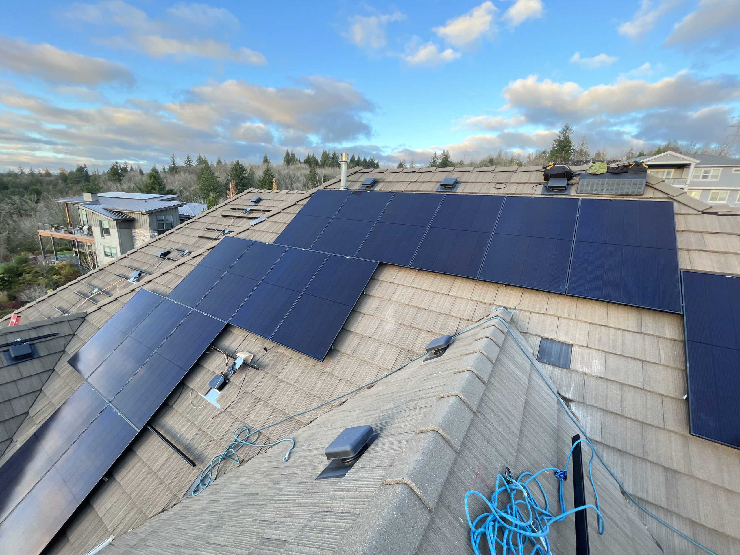 Residential solar installation on a concrete tile roof featuring black solar panels during construction.