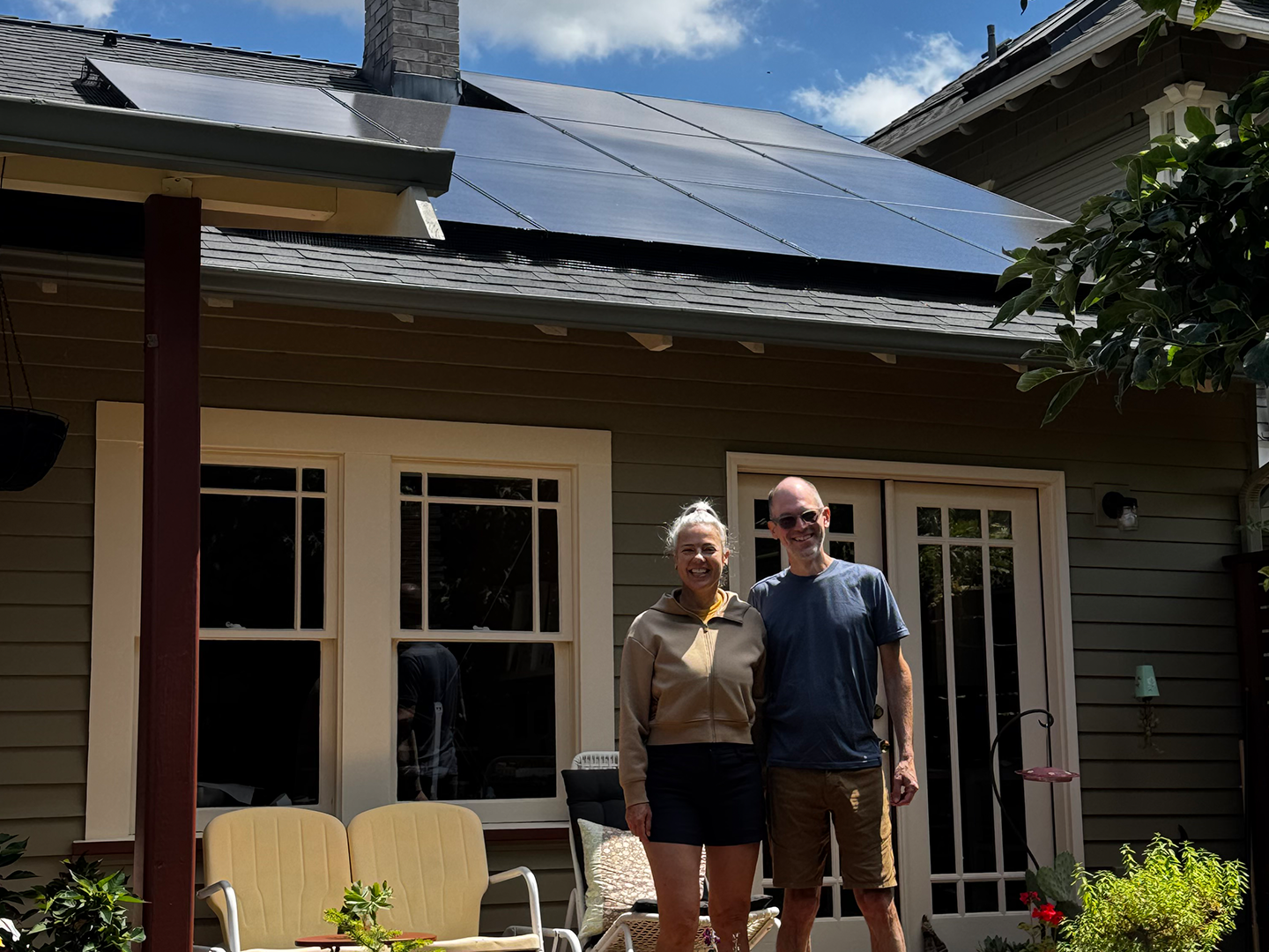 Homeowners standing on their backyard deck beneath a newly installed rooftop solar array on their Oregon home.