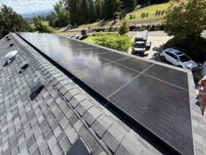 High-efficiency black solar panels installed on an asphalt shingle roof overlooking a residential neighborhood in Oregon.