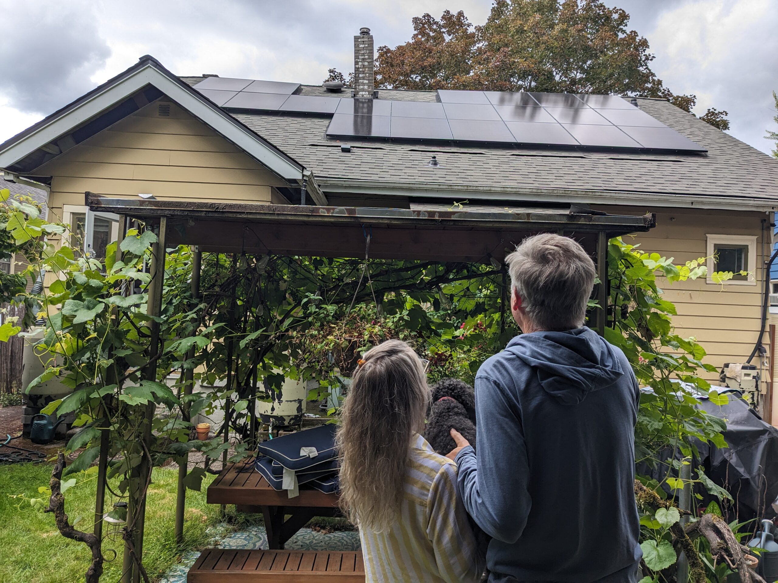 Homeowners standing in their backyard looking at newly installed rooftop solar panels on their home.