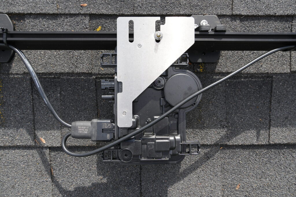 Close-up of an Enphase IQ8-MC microinverter mounted beneath the solar array on a shingle roof.