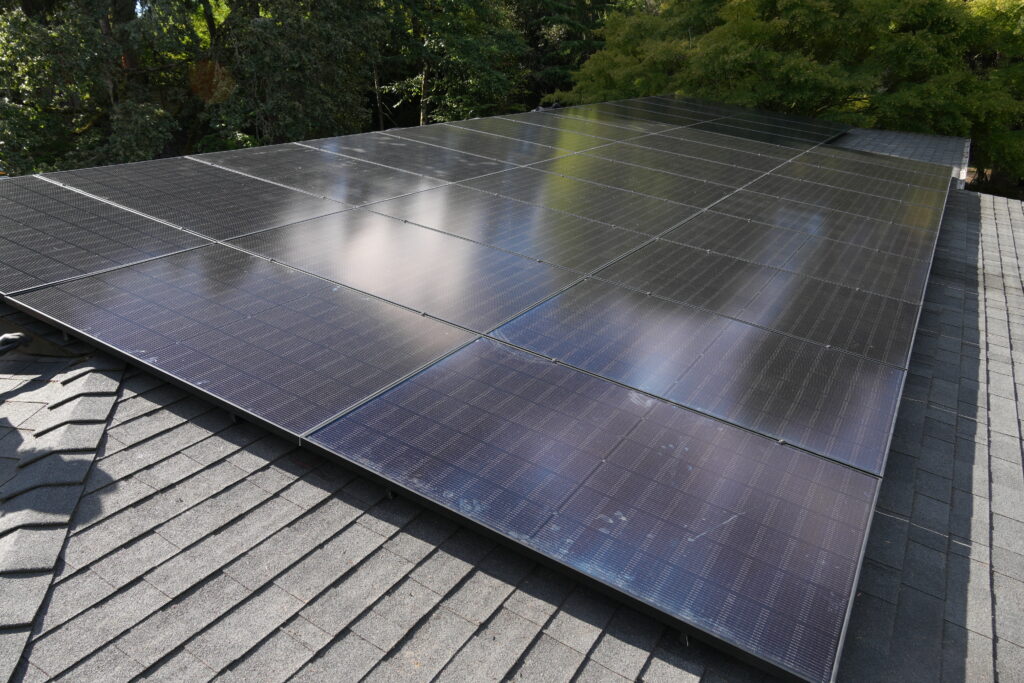 Finished array of black Silfab solar panels installed on a shingle roof surrounded by trees in Portland.
