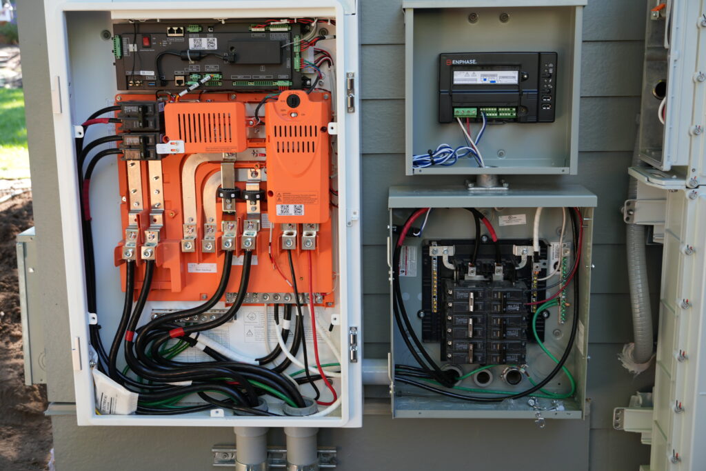 Open FranklinWH energy management system and Enphase solar monitoring equipment installed beside a residential electrical panel.