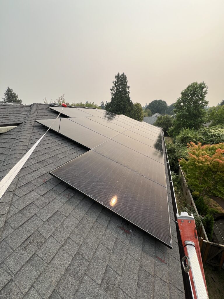 Black solar panels being installed on a residential asphalt shingle roof with safety equipment visible.
