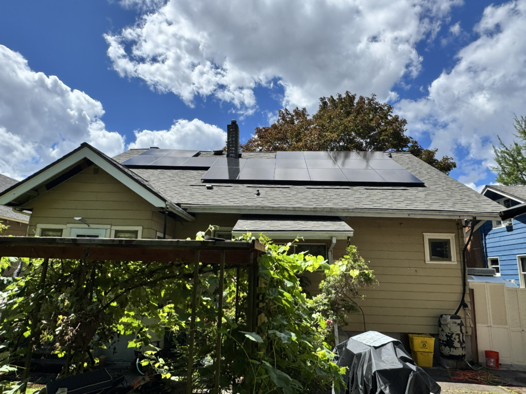 Solar panels installed on the roof of a residential home under a bright blue sky.