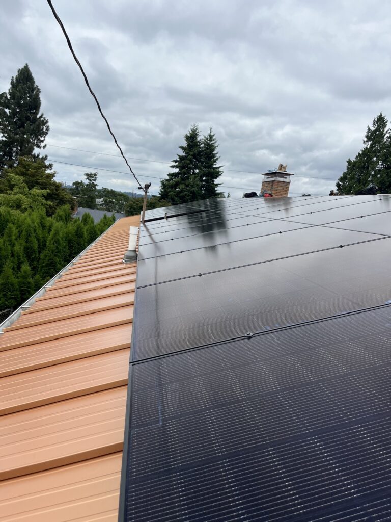 Black solar panels installed across a copper-colored standing-seam metal roof under cloudy skies.