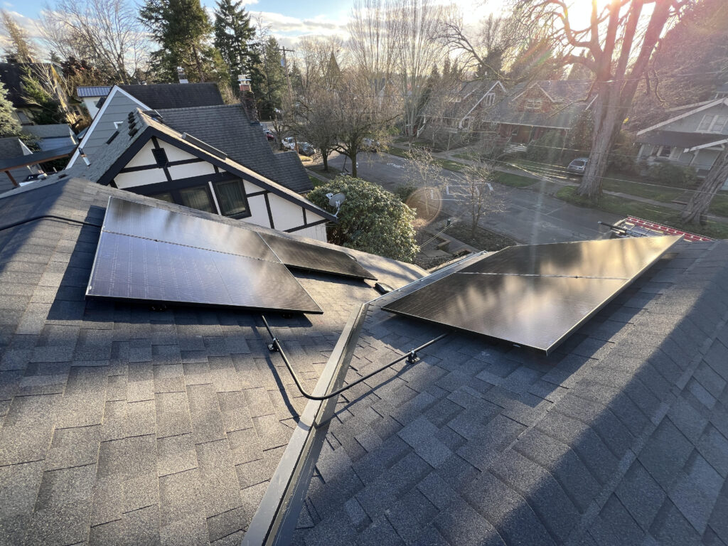 Black solar panels installed on multiple sections of a complex asphalt shingle roof on a Portland-area home.