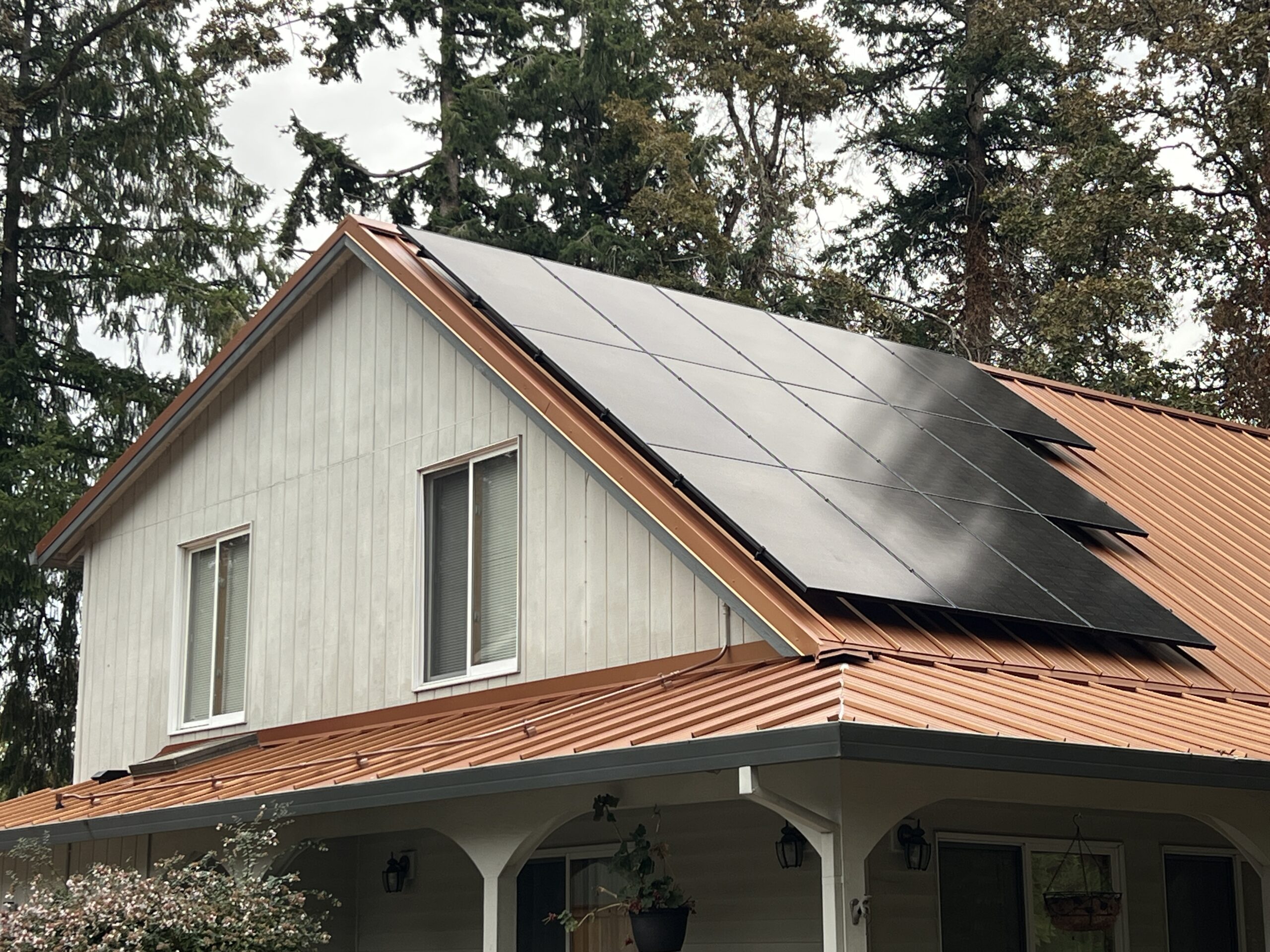 Dark solar panels on a warm-toned standing-seam metal roof above the porch of a Milwaukie home.